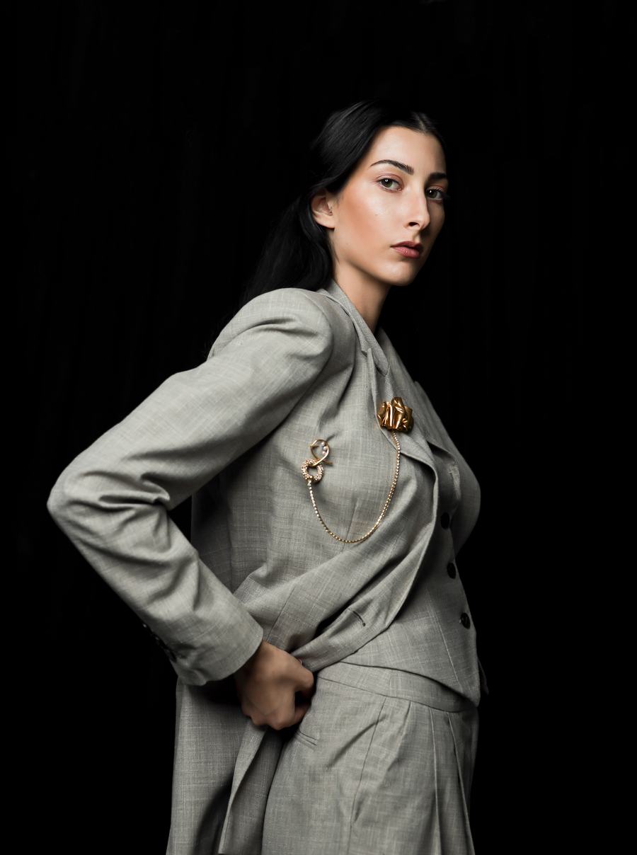 Grey tailoring with a gold brooch and chain against black