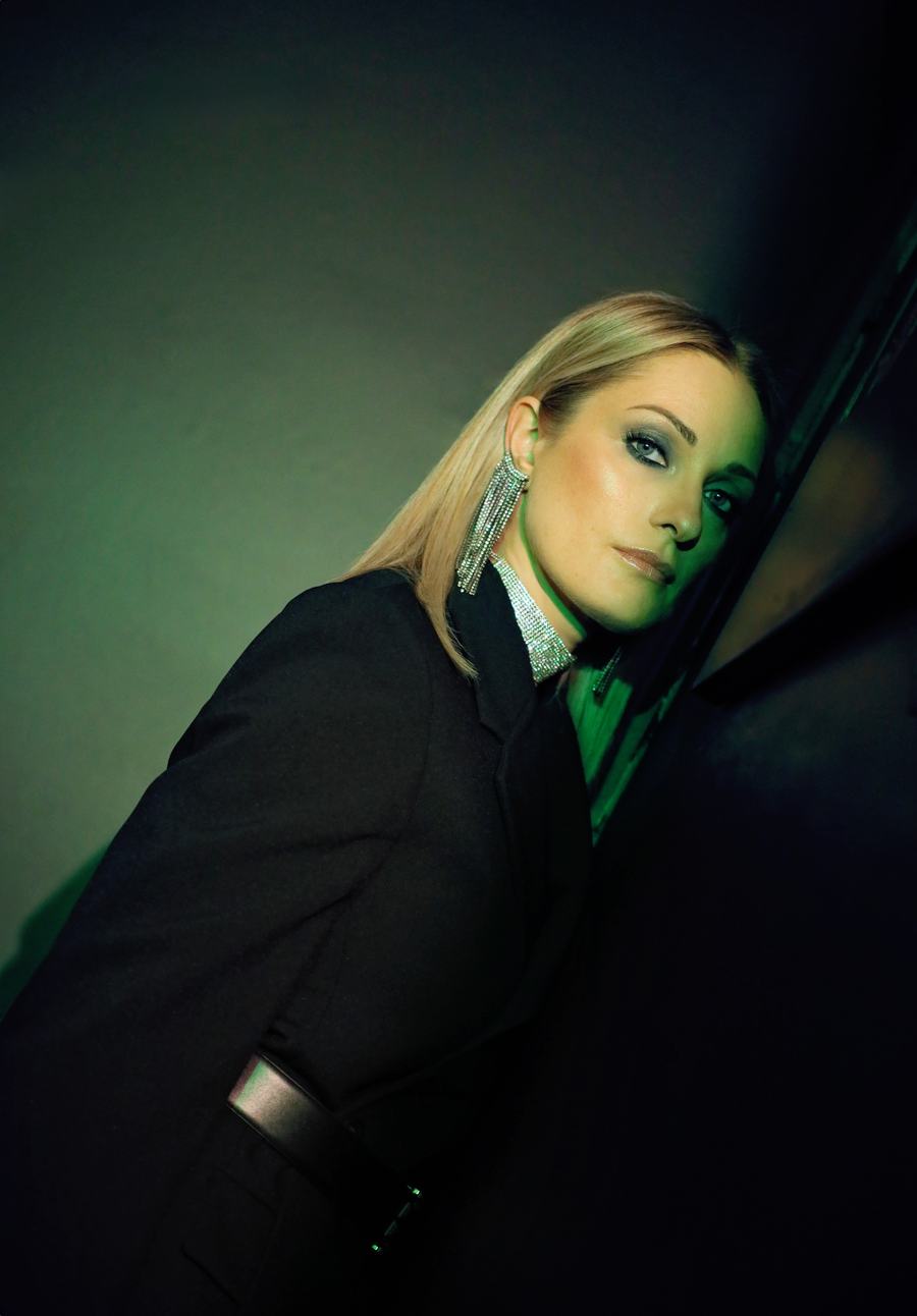 A black blazer and crystal earrings under green light