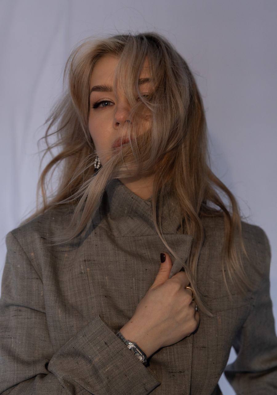 Wind-blown hair and a grey linen coat held at the collar