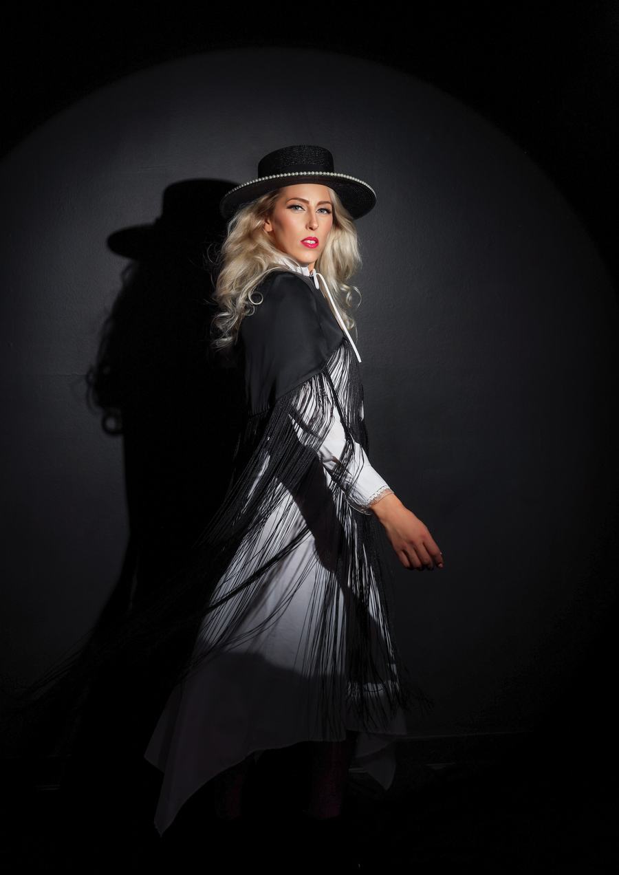 A figure in a black hat turning out of a pool of light, her shadow beside her