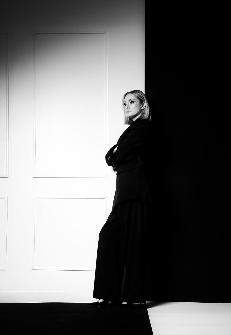 Black and white — a figure at a white door, split by a hard edge of shadow
