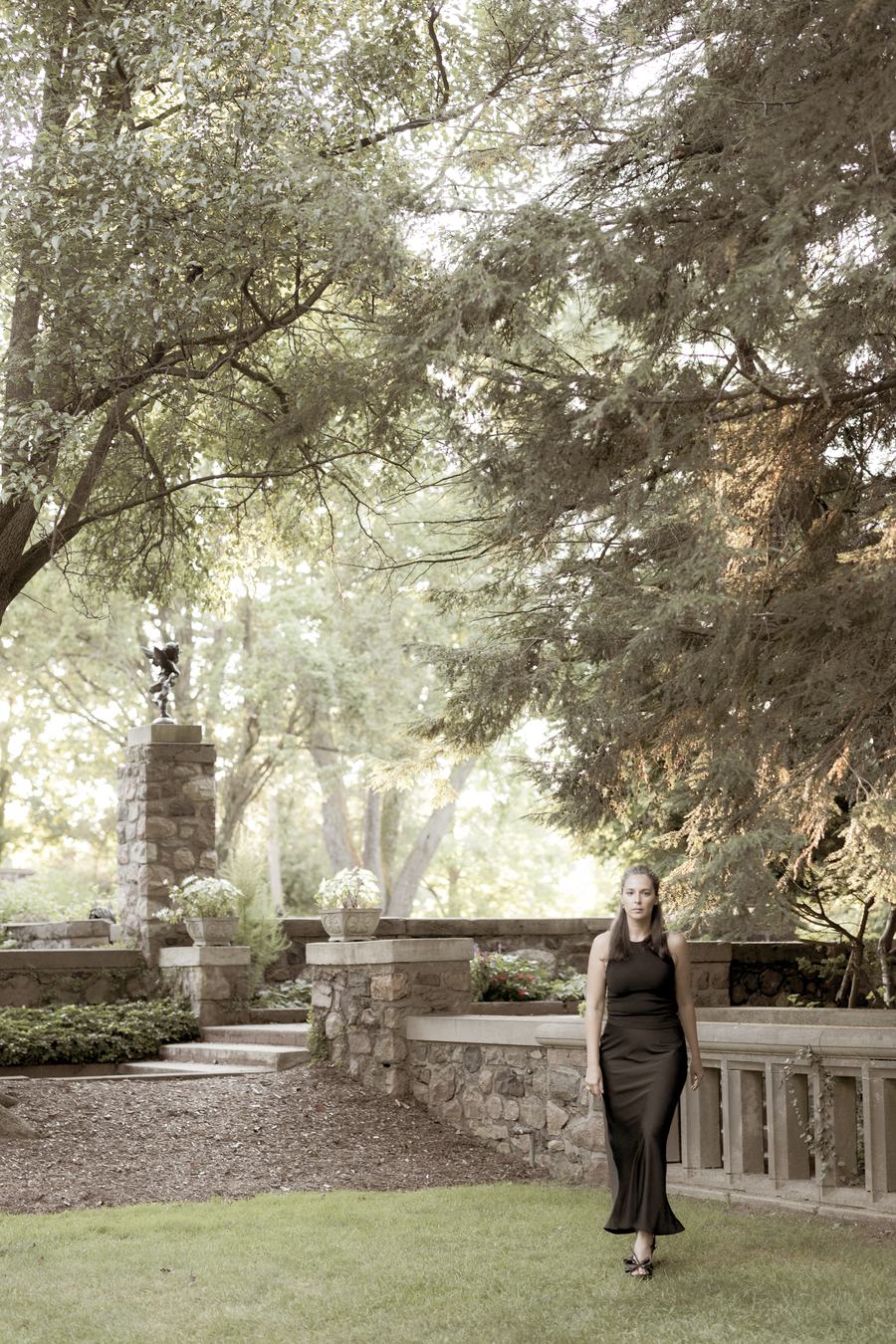 A small figure in black in a terraced stone garden under old trees