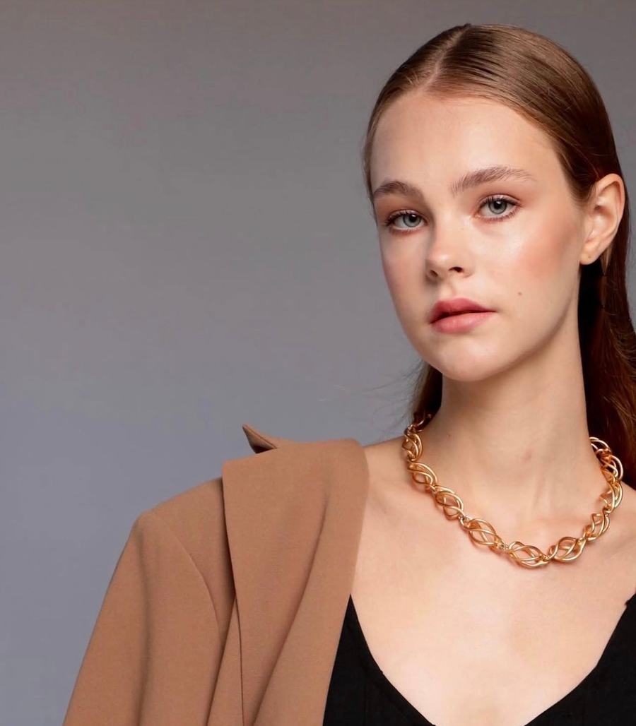 A camel jacket and gold chain against lilac grey