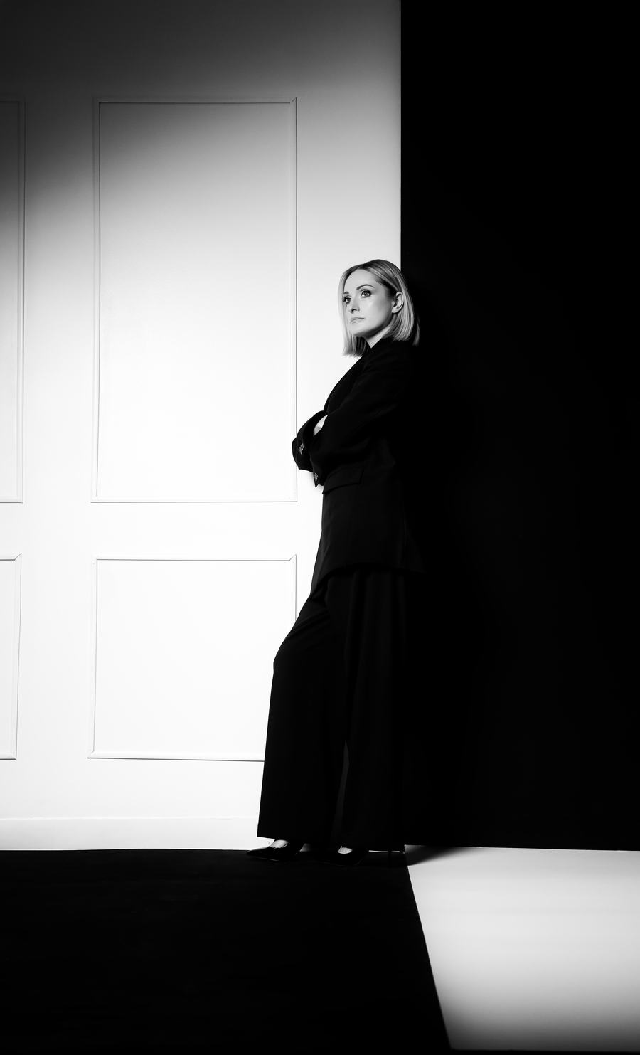 Black and white — a figure at a white door, split by a hard edge of shadow