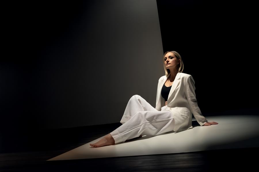 A woman in a white linen suit seated in a shaft of light
